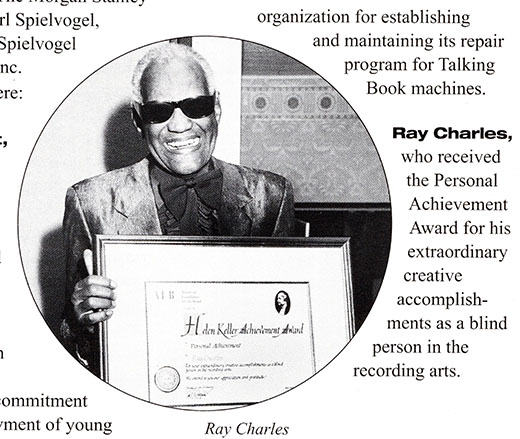 Ray Charles holds the Helen Keller Achievement Award, a large framed certifIcate. The certificate bears the AFB logo, an image of Helen Keller, a metallic seal, and two signatures. Charles is smilling and wears dark glasses and a shiny blazer with a large bow tie and matching button-down shirt.