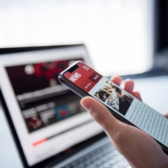 Online news on a smartphone and laptop, Woman reading news or articles in a mobile phone screen application at home. Newspaper and portal on internet.