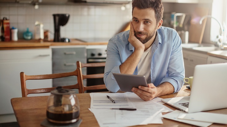 billede af en mand, der planlægger sin dag ved køkkenbordet med en computer