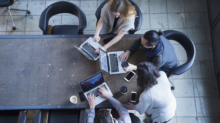 Aufsichtfoto von vier Personen, die an einem Tisch an Computern und Geräten arbeiten