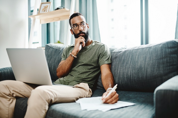 photo of a man sitting on a sofa with paper and a laptop