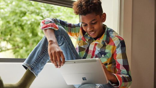 Un jeune étudiant masculin assis sur un appui de fenêtre regardant son appareil Surface Pro.
