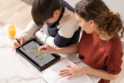 Seorang anak laki-laki bekerja di tablet sementara orang tua perempuannya melihat ke pundaknya