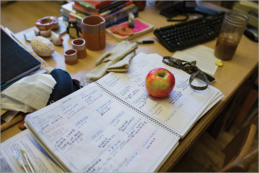 Uma mesa de educador com blocos de anotações, livros, uma maçã e café gelado.