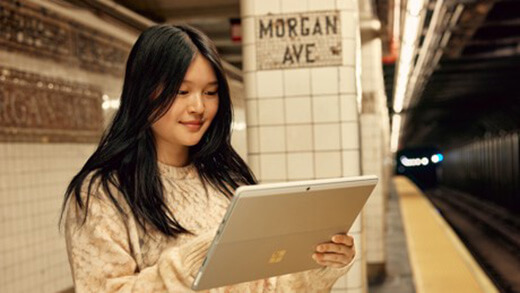 Uma mulher olha para seu dispositivo Surface Pro enquanto está em uma plataforma subterrânea do metrô.