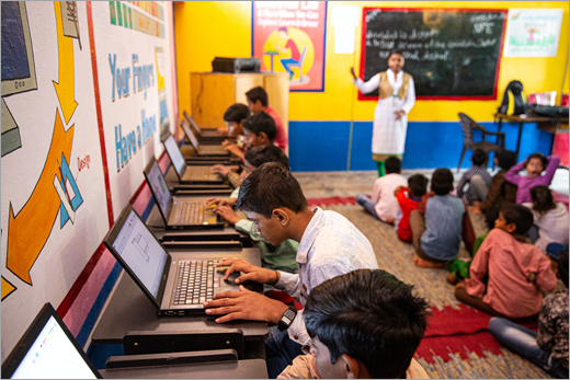 Um educador que se apresenta em uma escola na Índia enquanto os alunos trabalham em laptops.