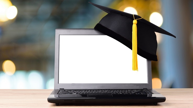 Fotografia de um boné de graduação e de um computador portátil