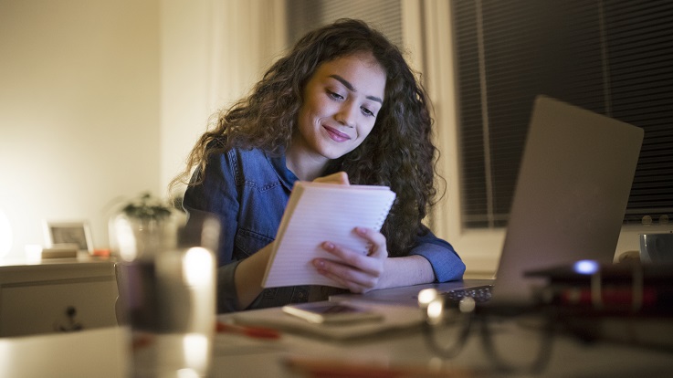 photo of a woman at a kitchen table with a jar of coins working on her budget